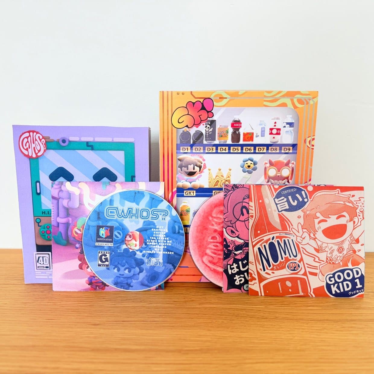 The contents of a Good Kid loot box laid out on a table: a CD, printed cards, sticker sheets and a poster