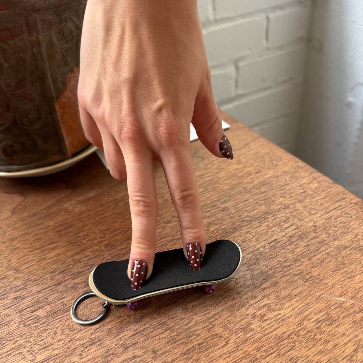 A hand balancing a printed fingerboard, a miniature skateboard, on a wooden table