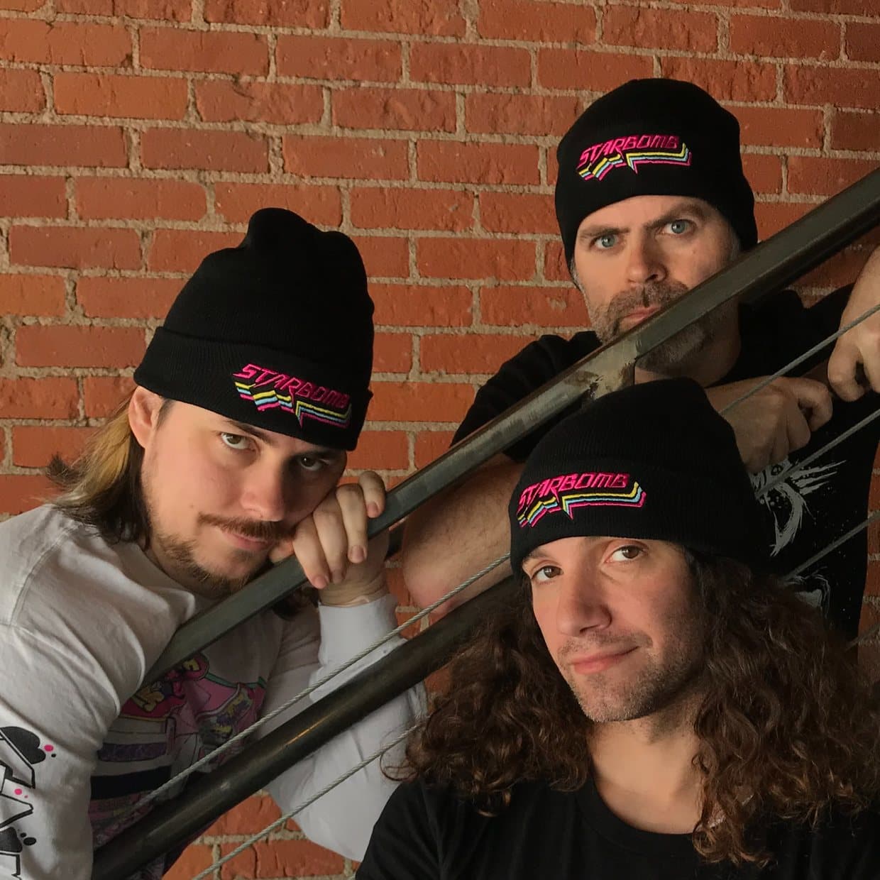 Two people leaning on an iron staircase against a brick wall, both in black Starbomb beanies